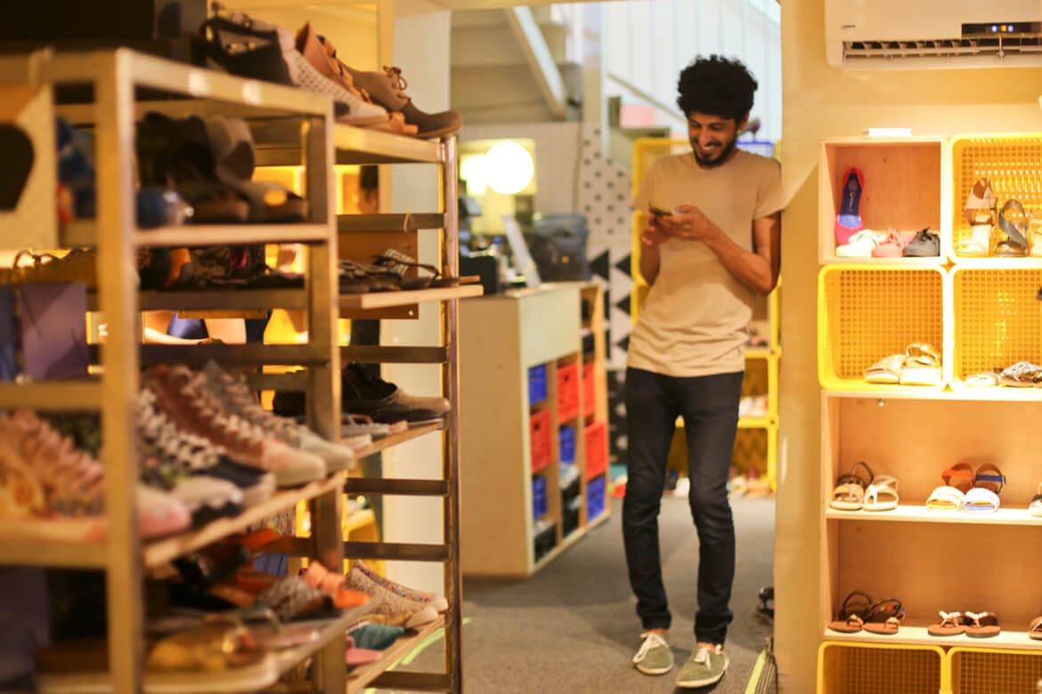 בחור עם שיער מקורזל מתבונן בטלפון שלו וצוחק בחנות שופרא בתל אביב